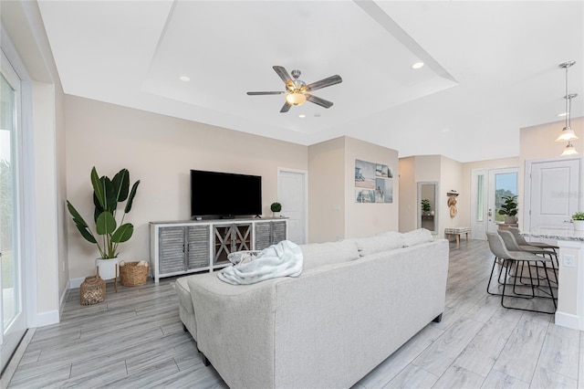 living room featuring a tray ceiling, light hardwood / wood-style floors, and ceiling fan