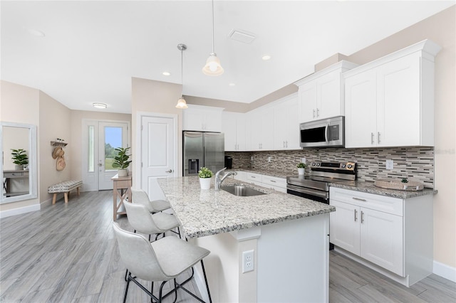 kitchen featuring appliances with stainless steel finishes, decorative light fixtures, an island with sink, sink, and white cabinets