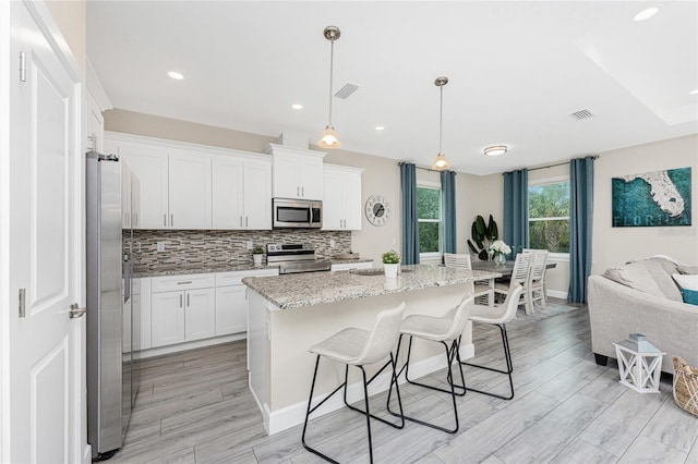 kitchen featuring a kitchen island with sink, light stone countertops, white cabinets, and appliances with stainless steel finishes