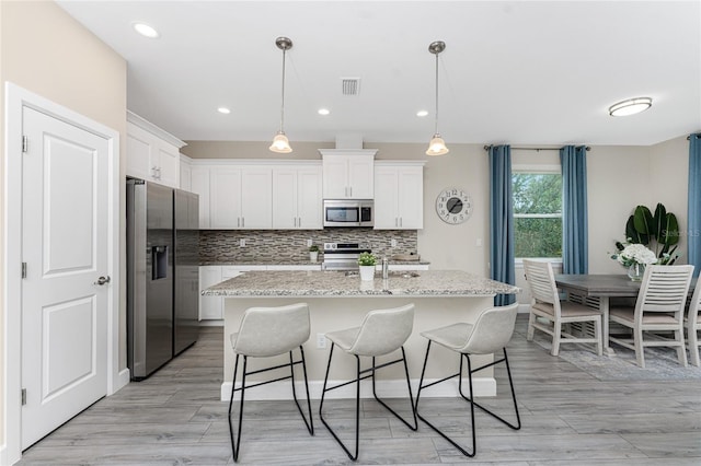 kitchen with white cabinetry, light stone counters, decorative light fixtures, a center island with sink, and appliances with stainless steel finishes