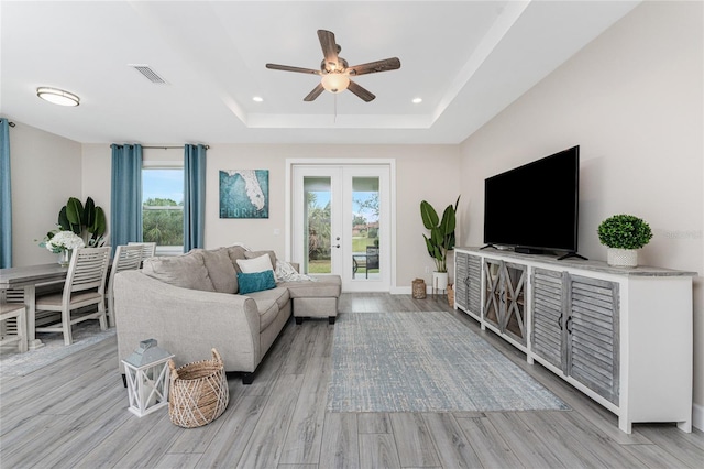 living room with french doors, ceiling fan, a tray ceiling, and light hardwood / wood-style floors