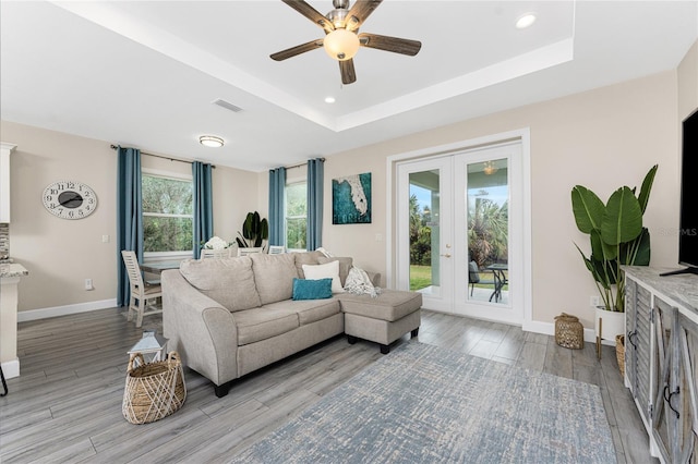 living room featuring a raised ceiling, ceiling fan, light wood-type flooring, and french doors