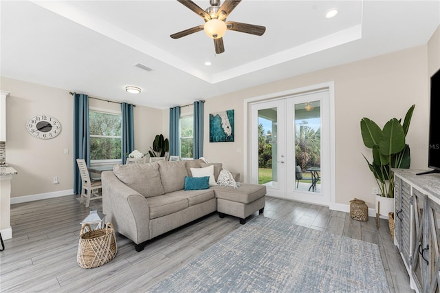 living room featuring french doors, ceiling fan, a raised ceiling, and light wood-type flooring