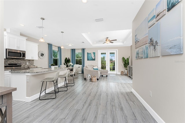 kitchen featuring white cabinetry, a kitchen bar, hanging light fixtures, stainless steel appliances, and light stone countertops