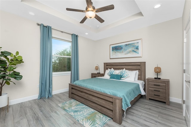 bedroom with ceiling fan, a tray ceiling, and light hardwood / wood-style floors