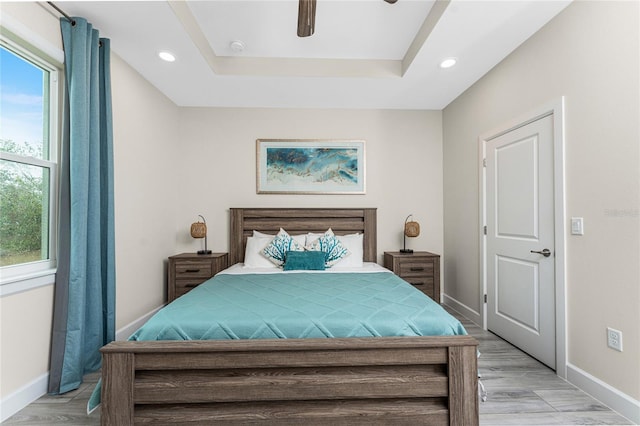 bedroom featuring ceiling fan, a raised ceiling, and light hardwood / wood-style flooring