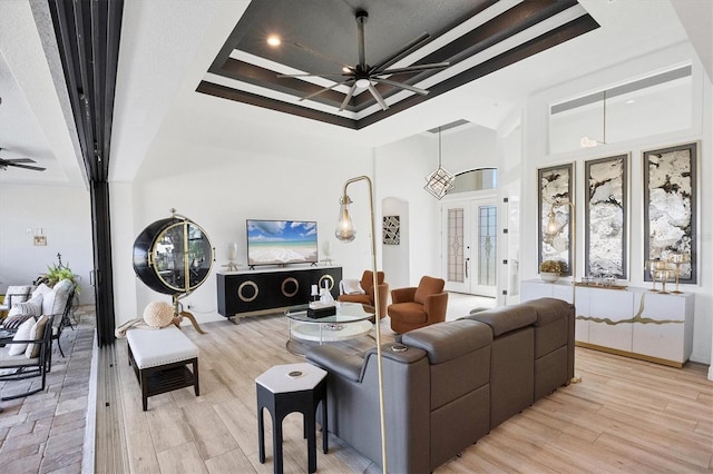 living room featuring a high ceiling, ceiling fan, a raised ceiling, light wood-type flooring, and french doors