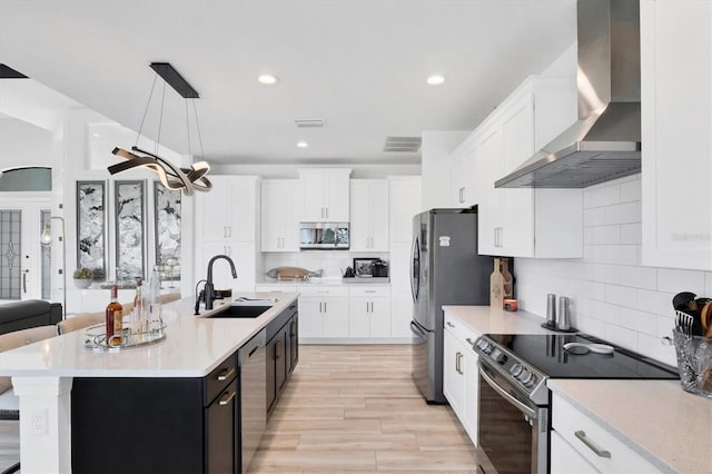 kitchen with sink, white cabinetry, decorative light fixtures, appliances with stainless steel finishes, and wall chimney range hood