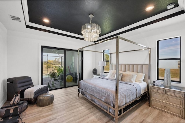 bedroom with access to outside, light hardwood / wood-style floors, a raised ceiling, and a chandelier