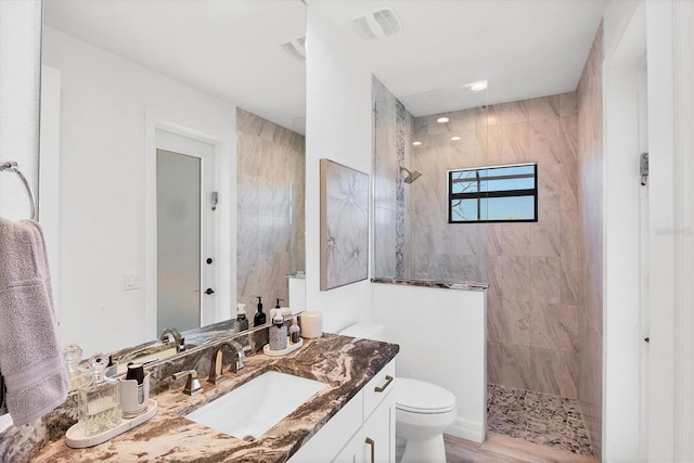 bathroom with a tile shower, vanity, and toilet