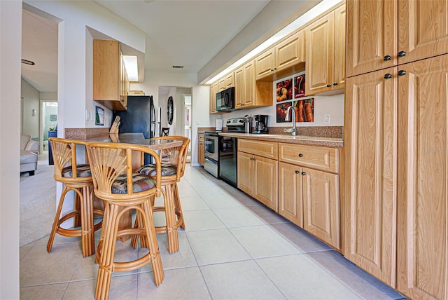 kitchen featuring a kitchen breakfast bar, light brown cabinetry, light tile patterned floors, and black appliances