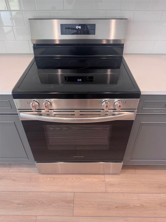 kitchen view of stainless steel range with electric stovetop, gray cabinets, light countertops, and decorative backsplash