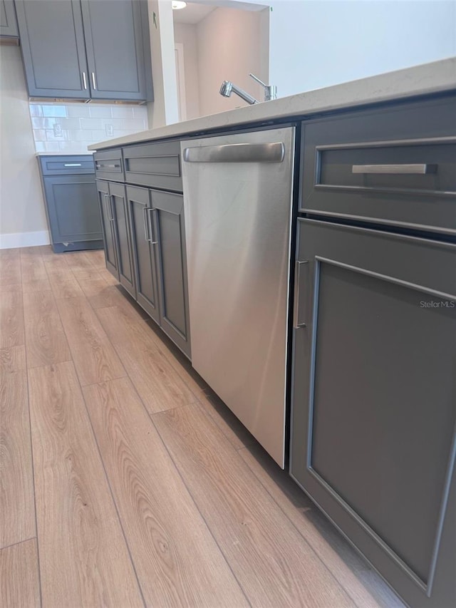 kitchen featuring stainless steel dishwasher, light wood-type flooring, backsplash, light countertops, and gray cabinets