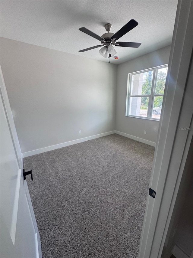 carpeted spare room with a textured ceiling, a ceiling fan, and baseboards