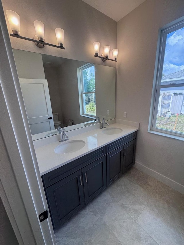 full bath with double vanity, toilet, and baseboards