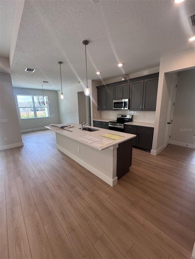 kitchen featuring stainless steel appliances, a sink, a textured ceiling, baseboards, and light wood-type flooring
