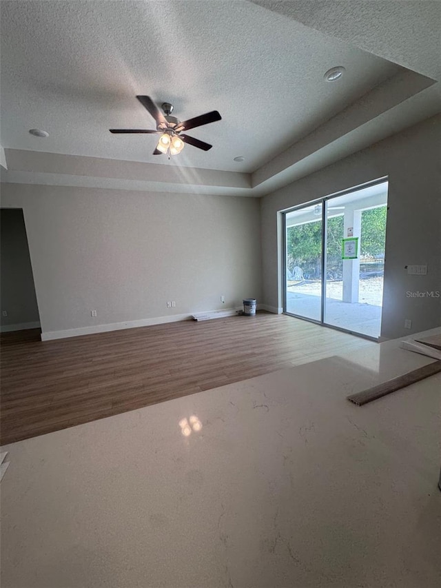 unfurnished living room with wood finished floors, a textured ceiling, ceiling fan, and baseboards