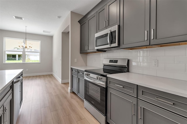2814 Vogler Ln, North Port, FL 34286 - kitchen with appliances with stainless steel finishes, decorative backsplash, a chandelier, light countertops, and gray cabinetry