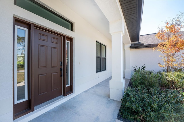 entrance to property featuring covered porch, stucco siding, and roof with shingles