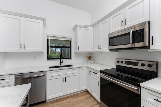 kitchen featuring light stone counters, stainless steel appliances, light wood-style floors, white cabinetry, and a sink