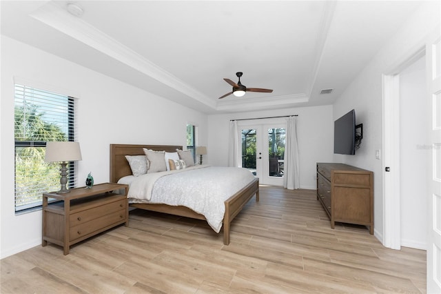 bedroom with access to exterior, a tray ceiling, light hardwood / wood-style floors, and french doors