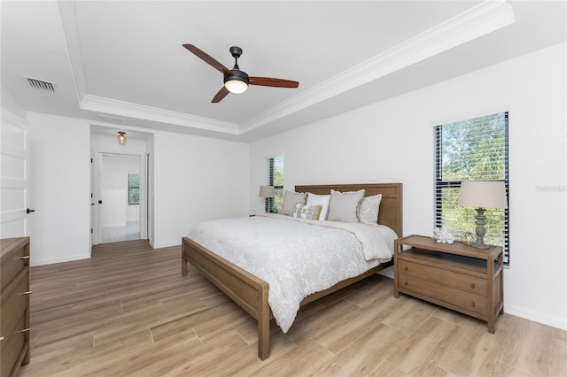 bedroom featuring light wood finished floors, visible vents, crown molding, and a raised ceiling