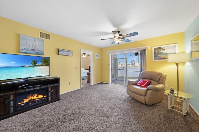 carpeted living area with ceiling fan, visible vents, baseboards, and a glass covered fireplace