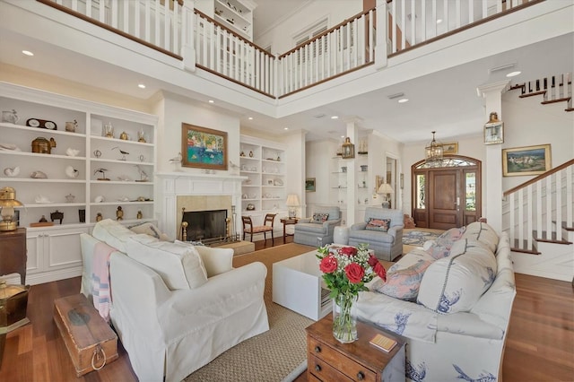 living room with a tile fireplace, built in features, a high ceiling, crown molding, and dark wood-type flooring