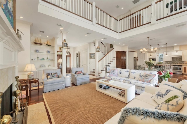 living room featuring built in features, a high ceiling, a notable chandelier, a fireplace, and wood-type flooring