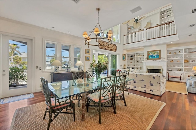 dining space with a towering ceiling, built in features, a chandelier, hardwood / wood-style flooring, and crown molding