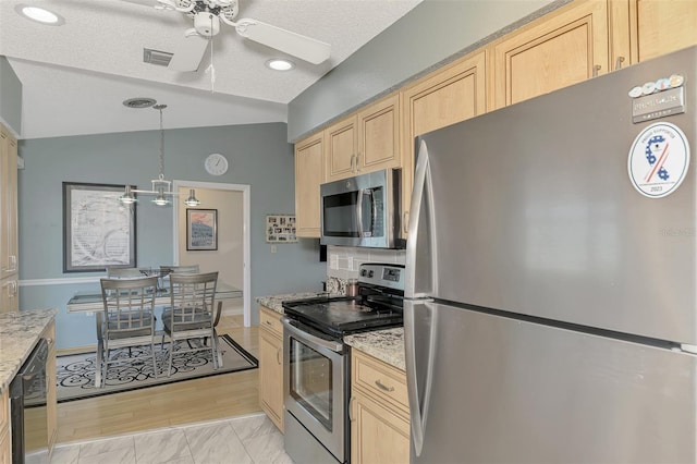 kitchen featuring vaulted ceiling, light brown cabinetry, decorative light fixtures, stainless steel appliances, and light stone countertops