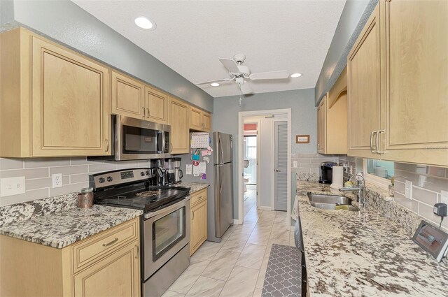 kitchen featuring light stone counters, stainless steel appliances, light brown cabinetry, and sink