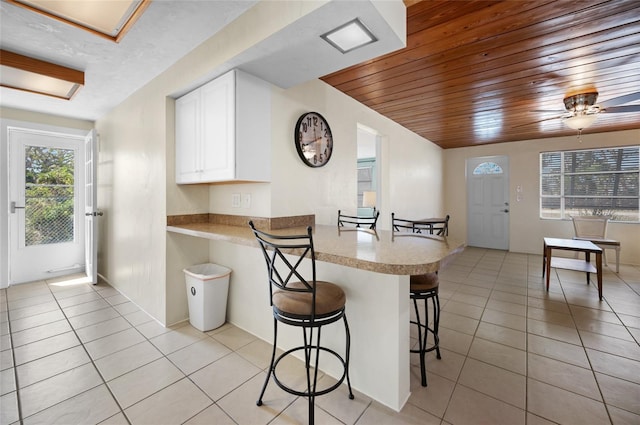 kitchen with light tile patterned floors, a kitchen breakfast bar, white cabinets, wooden ceiling, and kitchen peninsula