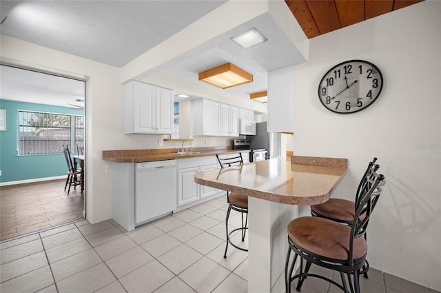 kitchen featuring a breakfast bar, light tile patterned floors, kitchen peninsula, white appliances, and white cabinets