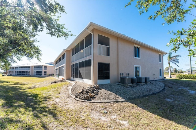 rear view of house featuring central AC unit, a lawn, and a sunroom