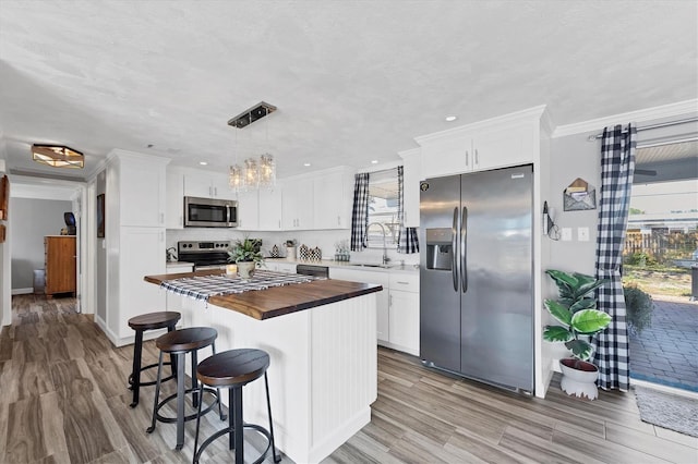 kitchen featuring pendant lighting, wooden counters, white cabinetry, stainless steel appliances, and a kitchen island