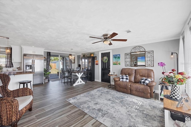 living room featuring dark wood-type flooring, ceiling fan with notable chandelier, and a textured ceiling