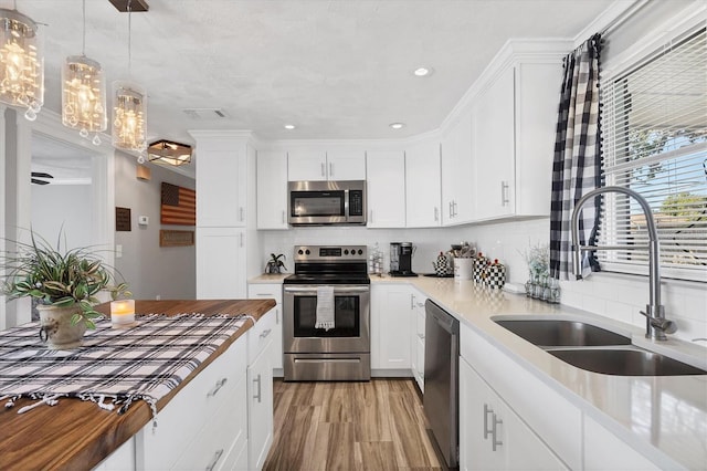 kitchen featuring sink, appliances with stainless steel finishes, white cabinetry, hanging light fixtures, and decorative backsplash