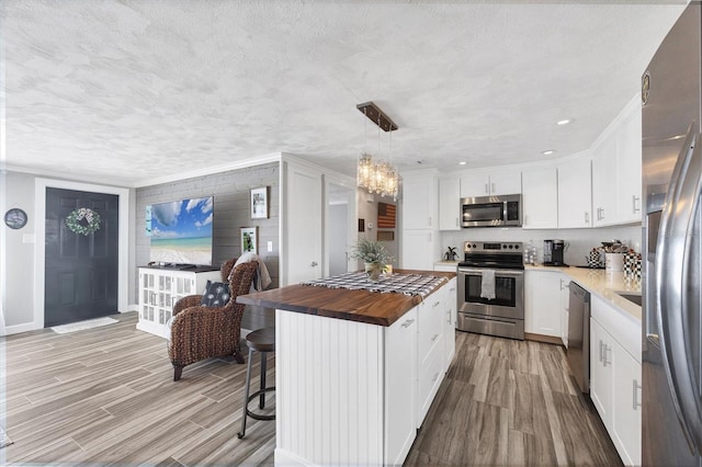 kitchen with a kitchen island, appliances with stainless steel finishes, wood counters, white cabinetry, and hanging light fixtures