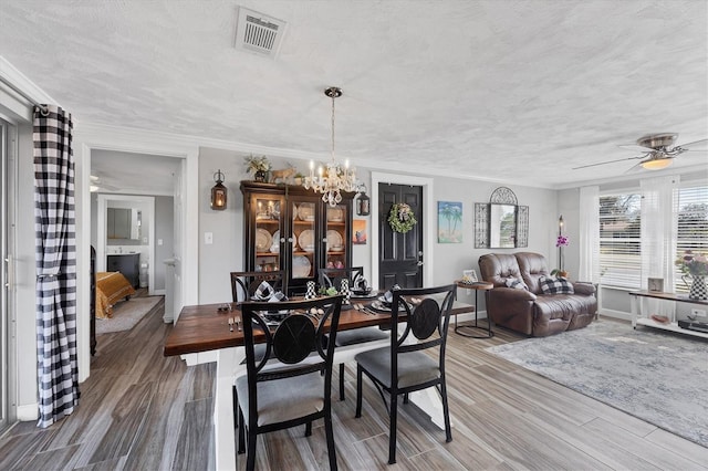 dining room featuring hardwood / wood-style flooring, crown molding, ceiling fan with notable chandelier, and a textured ceiling