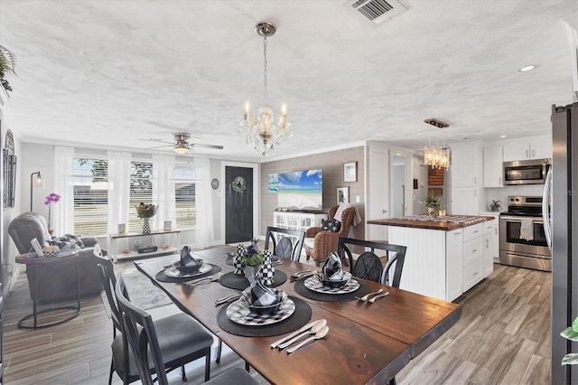 dining room with ceiling fan with notable chandelier, ornamental molding, light hardwood / wood-style floors, and a textured ceiling