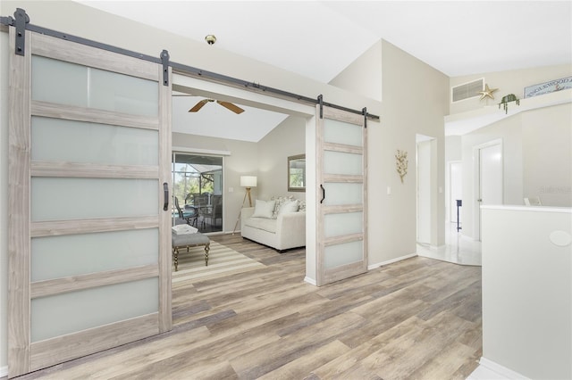 unfurnished living room featuring hardwood / wood-style flooring, ceiling fan, a barn door, and high vaulted ceiling