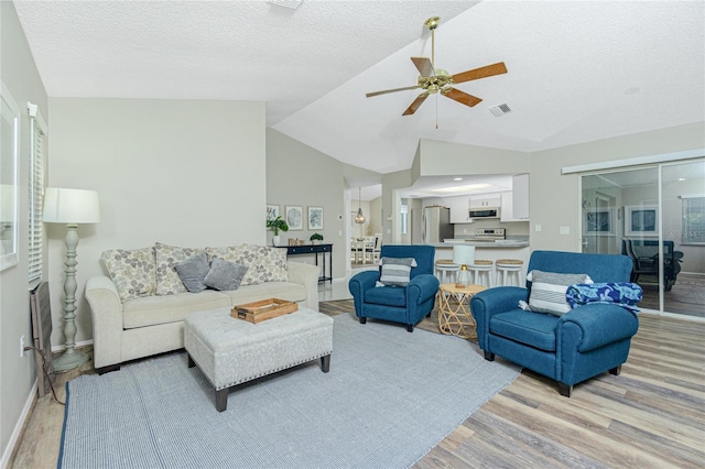 living room with lofted ceiling, a textured ceiling, light hardwood / wood-style flooring, and ceiling fan