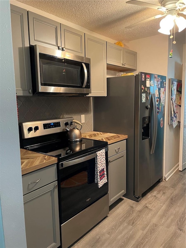 kitchen with gray cabinets, backsplash, light hardwood / wood-style floors, stainless steel appliances, and a textured ceiling