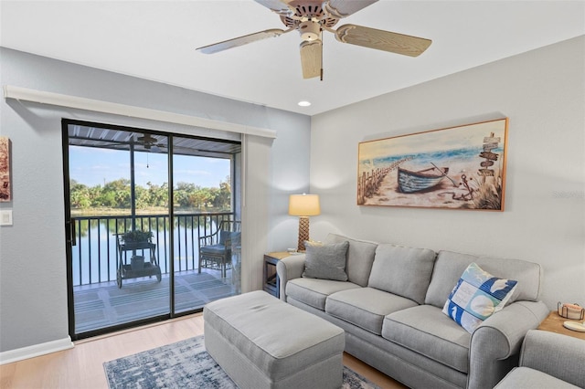 living room featuring light hardwood / wood-style floors, ceiling fan, and a water view