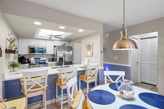 kitchen with a breakfast bar, white cabinetry, a skylight, stainless steel appliances, and decorative light fixtures