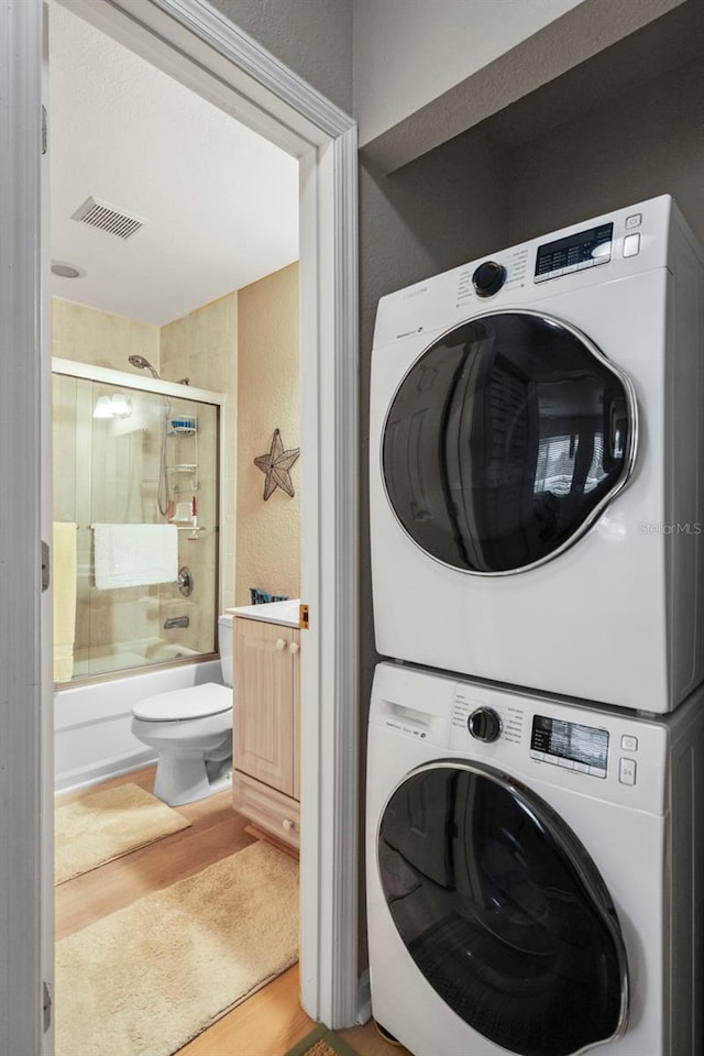 clothes washing area with hardwood / wood-style flooring and stacked washer and clothes dryer