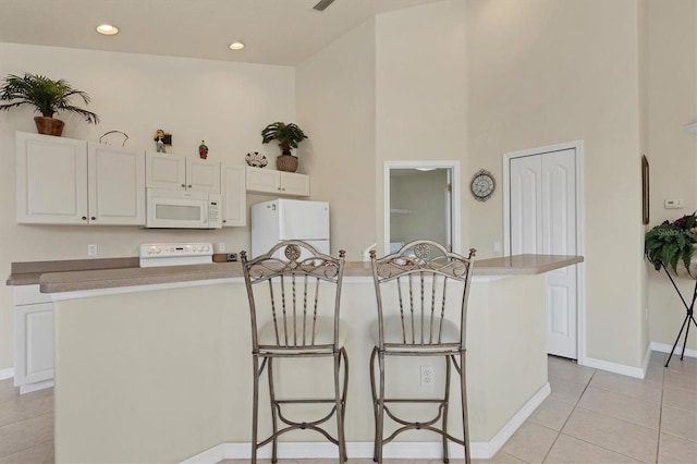 kitchen featuring a towering ceiling, white cabinetry, a center island, light tile patterned floors, and white appliances