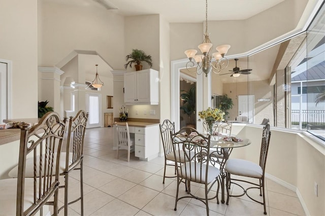 dining space featuring a towering ceiling, ceiling fan with notable chandelier, ornate columns, and light tile patterned flooring