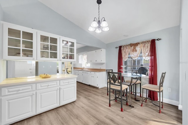 kitchen with lofted ceiling, hanging light fixtures, white dishwasher, white cabinets, and light wood-type flooring